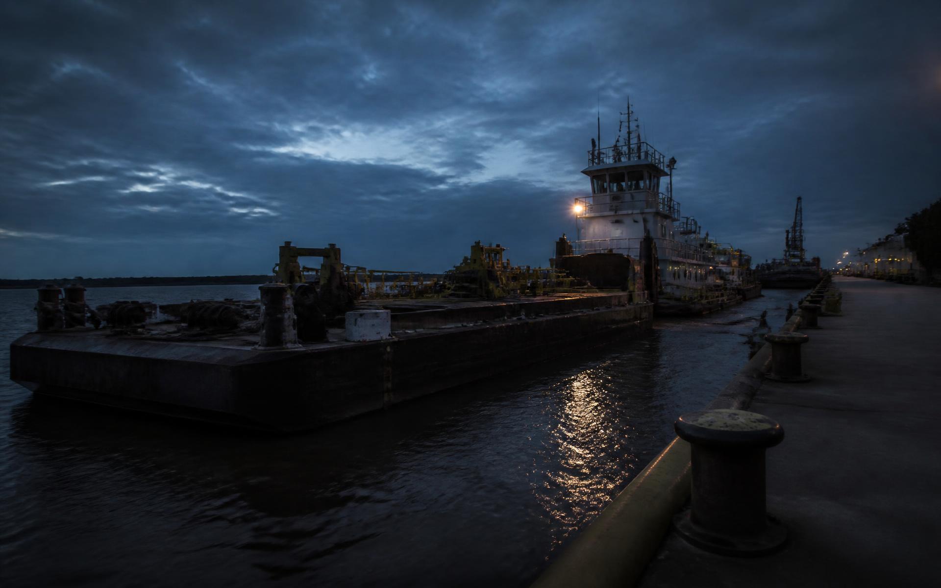 Barge and workboat moored along an industrial waterfront at dusk